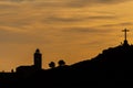 Silhouette of people and dog on top of a hill with a large cross with a church and trees in the background