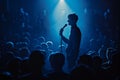 Silhouette of performer on stage, microphone in hand, addressing a large audience under dramatic blue lighting. Captured Royalty Free Stock Photo
