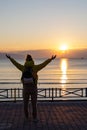 Silhouette of a person with arms raised, greeting the sunrise by the sea.