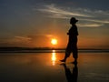 Silhouette of a woman walking alone with bare feet in the beach at sunset. Royalty Free Stock Photo