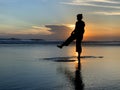 Silhouette of the person dancing alone in the beach at sunset. A woman having fun with the sea water reflection and sunlight.