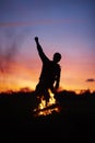 Silhouette of a person dancing with a blurry background and a campfire during a beautiful sunset