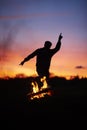 Silhouette of a person dancing with a blurry background and a campfire during a beautiful sunset
