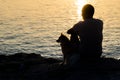 Silhouette of person and dog sitting together at seaside and looking at the sunrise. Friendshep of a man and animal Royalty Free Stock Photo