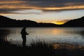 silhouette of a person fly fishing against a mountain lake sunset Royalty Free Stock Photo