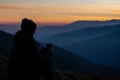silhouette of a person holding coffee, dawn breaking over the mountains