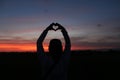 Silhouette of a person holding a heart shaped hands. Person making love sign against colorful romantic sunset sunrise sky clouds Royalty Free Stock Photo