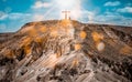 Silhouette of a person praying on top of a mountain near the cross with sun shining in blue sky