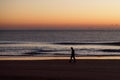 Silhouette of a Person Strolling along a Quiet Beach with Pastel Horizon at Sunrise Royalty Free Stock Photo
