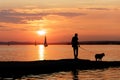 Silhouette of a person walking his dog on a beach one day with a red sunset. Royalty Free Stock Photo