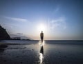 Silhouette of a person walking on a reflective beach under a starry twilight sky with a bright Royalty Free Stock Photo