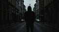 A silhouette of a person wearing a hoodie stands in the center of an urban street.