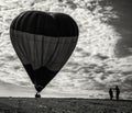 Silhouette of persons holding a flying hot-air balloon on the ground