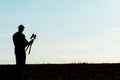 The silhouette of a photographer with a camera and a tripod in his hands in front of the sun. A photographer takes pictures of a Royalty Free Stock Photo