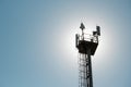 Silhouette of a platform with transmitters on a cellular tower against the background of the sky and the sun on a summer day