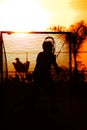Silhouette player holding Sunset Lacrosse Sticks near the net for the game under an orange sunlight