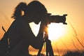 Silhouette portrait of a young woman photographing a beautiful nature at sunset on photo equipment