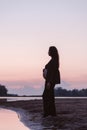 Silhouette of pregnant woman on beach. Beautiful young brunette with long curly hair stands on sand on beach and enjoys Royalty Free Stock Photo