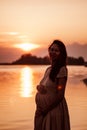 Silhouette of pregnant woman. Smiling, happy young woman in light dress enjoys rays of the setting sun, stands in water Royalty Free Stock Photo