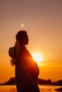 The silhouette of a pregnant woman at sunset. The silhouette of a young woman in a straw hat holding her pregnant belly Royalty Free Stock Photo