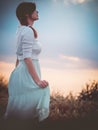 Silhouette profile of a beautiful girl in a dress in the field enjoying the sky during sunset, a young woman walking in nature, Royalty Free Stock Photo