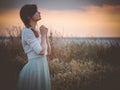 Silhouette profile of a beautiful girl in a dress praying to God in the field, a young woman walking on nature during sunset Royalty Free Stock Photo