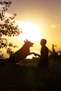 Silhouette profile of hapy man and dog sitting and playing on nature, boy training German Shepherd at sunset in a field, concept Royalty Free Stock Photo