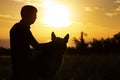 Silhouette profile of a young man and a dog watching the sun set on the horizon in a field, boy fondle his pet on nature, concept