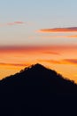 Silhouette of pyramid shaped hill and vividly colored evening sky in background