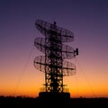 Silhouette of a radar tower with multiple dish-like structures stacked vertically, supported by a metal framework and cables. Royalty Free Stock Photo