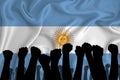 Silhouette of raised arms and clenched fists on the background of the flag of Argentina. The concept of power, power, conflict.