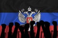 Silhouette of raised arms and clenched fists on the background of the flag of Donetsk People`s Republic. The concept of power,