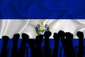 Silhouette of raised arms and clenched fists on the background of the flag of Salvador. The concept of power, conflict. With