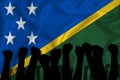 Silhouette of raised arms and clenched fists on the background of the flag of Solomon Islands. The concept of power, conflict.