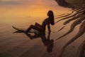 Silhouette and reflection of girl sitting on surfboard at ocean beach on background of beautiful sunset Royalty Free Stock Photo