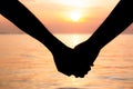 Silhouette of romantic couple holding hands and watching a beautiful sunset on the seashore. Love and valentine concept