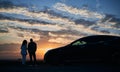 Loving pair with car watching romantic atmosphere of sunset. Royalty Free Stock Photo