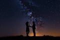 Silhouette of a romantic young couple with the man proposing at night against beautiful starry sky