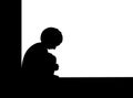 Silhouette of a sad child boy sitting on the floor, he hugging knees and bend down the head