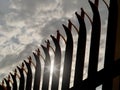 Silhouette of a security anti climbing fence with the sun shining through. Dramatic dark cloudy sky Royalty Free Stock Photo