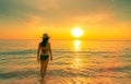 Silhouette woman walking at tropical sea with beautiful sunset sky at paradise beach. Happy girl wear bikini and straw hat Royalty Free Stock Photo