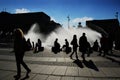 Silhouette shot of people in a fountain park near buildings on a cloudy daylight