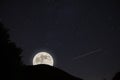 Silhouette shot of a tree, a hill with glowing full moon and shooting star in a starry night sky Royalty Free Stock Photo