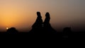 Silhouette shot of two people riding a camel in Dubai desert with sunset sky on the horizon Royalty Free Stock Photo