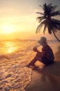 Silhouette side view of happy beautiful young woman wear straw hat - sit on the beach in summer at sunset time