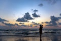 The silhouette of a single woman using a selfie to take a picture of herself By the sea at sunset