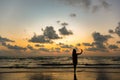 The silhouette of a single woman using a selfie to take a picture of herself By the sea at sunset