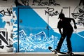 Silhouette of a skateboarder performing a freestyle maneuver against a wall with graffiti.