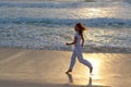 Silhouette of a slender woman jogging along the edge of the waves on the sandy sea beach at sunset