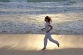 Silhouette of a slender woman jogging along the edge of the waves on the sandy sea beach at sunset